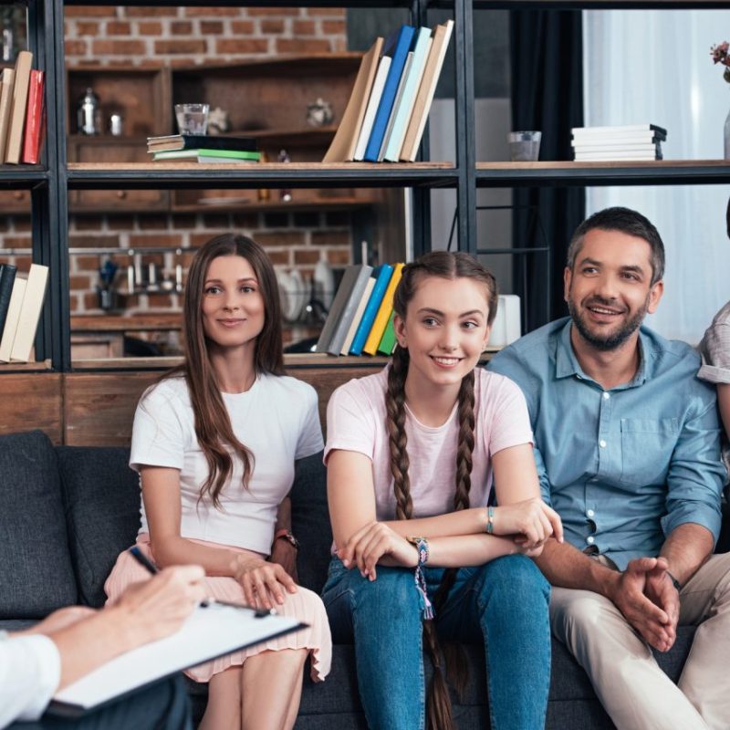 smiling-family-on-therapy-session-by-female-counselor-writing-in-clipboard-in-office